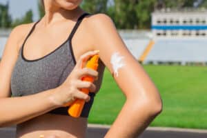 female runner standing and putting sun lotion on hand.
